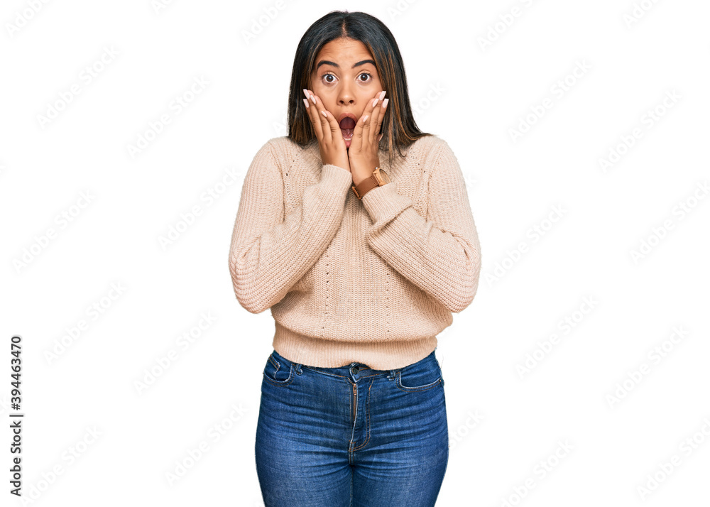 Young latin girl wearing wool winter sweater afraid and shocked, surprise and amazed expression with hands on face Young latin girl wearing wool winter sweater afraid and shocked, surprise and amazed expression with hands on face