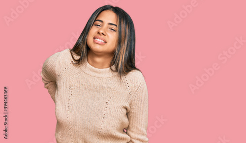 Young latin girl wearing wool winter sweater suffering of backache, touching back with hand, muscular pain