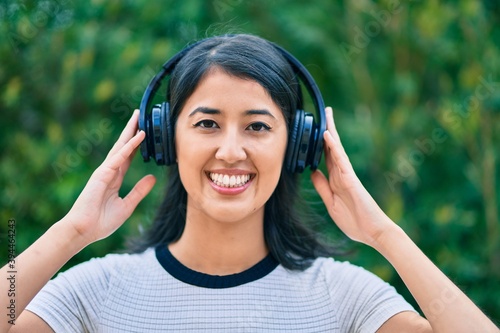 Young hispanic woman smiling happy listening to music using headphones at the city.