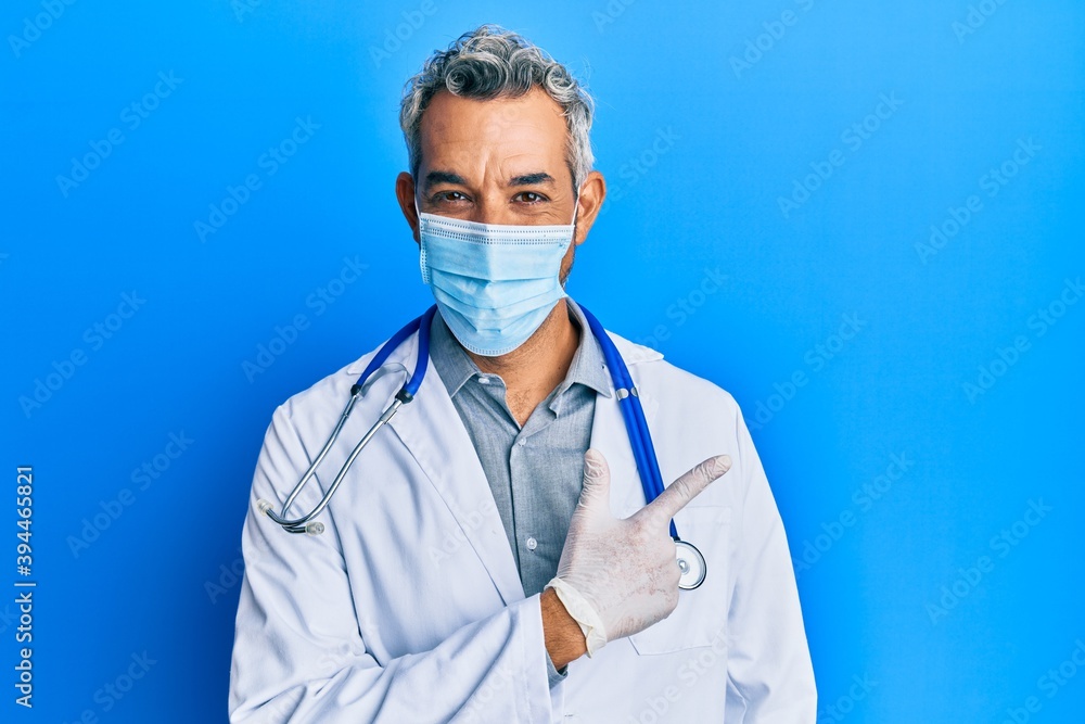Middle age grey-haired man wearing doctor uniform and medical mask smiling cheerful pointing with hand and finger up to the side Middle age grey-haired man wearing doctor uniform and medical mask smiling cheerful pointing with hand and finger up to the side