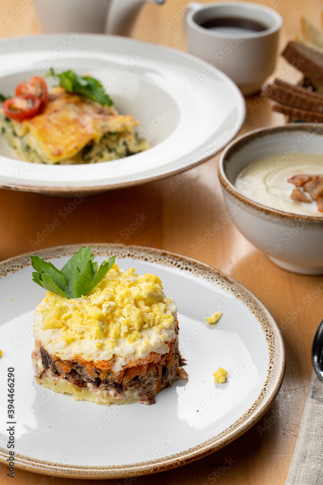 Traditional russian salad mimosa with boiled vegetables, fish, mayonnaise and grated egg, restaurant serving Traditional russian salad mimosa with boiled vegetables, fish, mayonnaise and grated egg, restaurant serving
