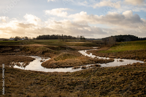 Overflowing river forms a bend in a rural landscape. Patches of sunlight shines on the scene with nice clouds at the horizon