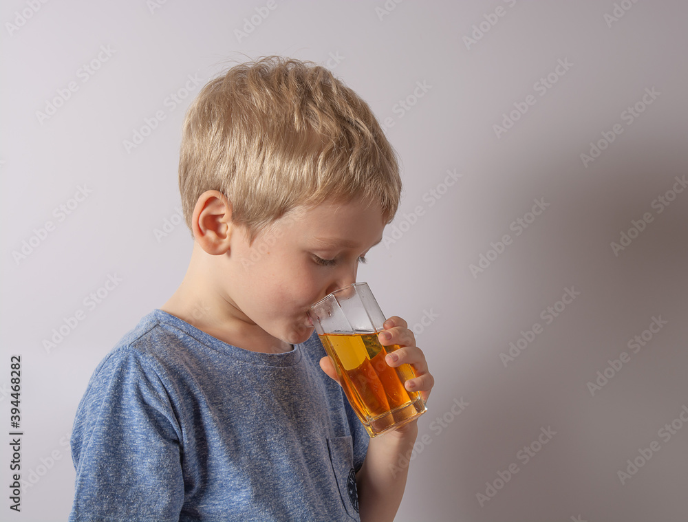 boy with blond hair drinks apple juice on gray background boy with blond hair drinks apple juice on gray background