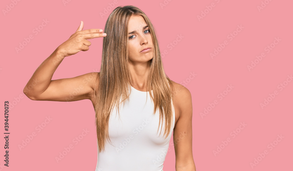 Young blonde woman wearing casual style with sleeveless shirt shooting and killing oneself pointing hand and fingers to head like gun, suicide gesture. Young blonde woman wearing casual style with sleeveless shirt shooting and killing oneself pointing hand and fingers to head like gun, suicide gesture.