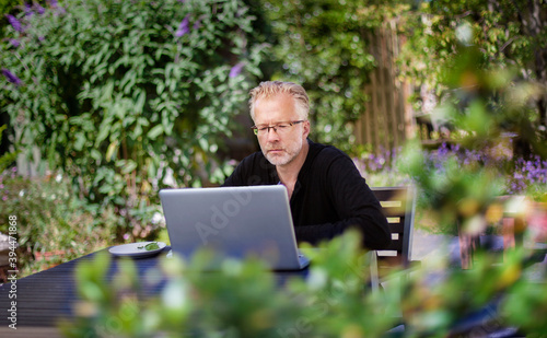 Man using laptop in garden, Denmark photo