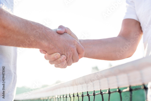 Midsection of men shaking hands while standing at tennis court against clear sky