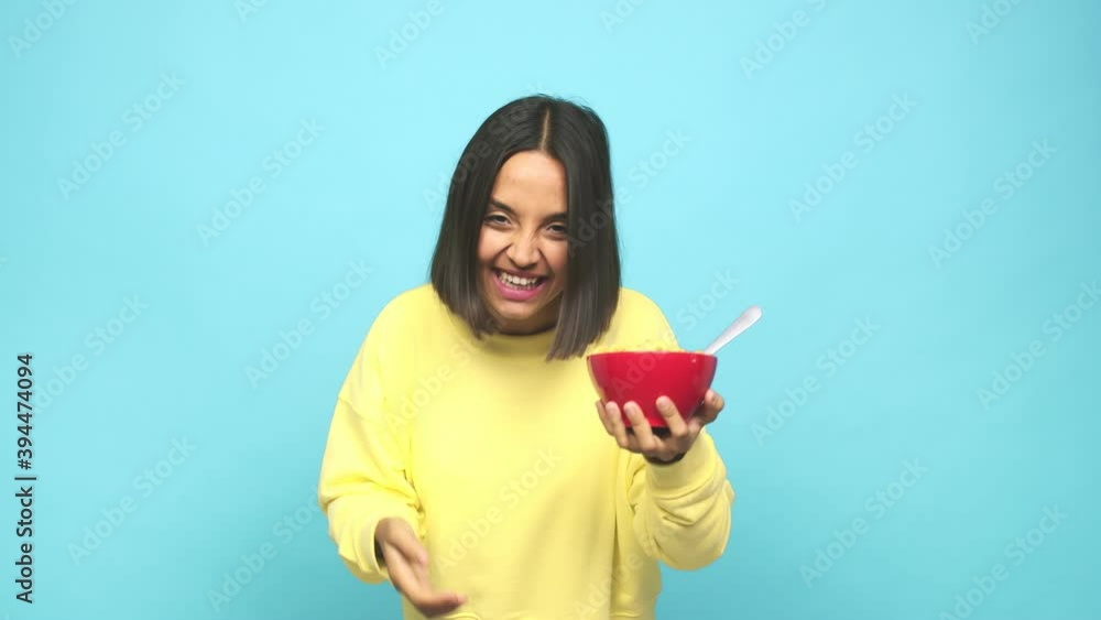 Young latin woman eating a cereals bowl receiving a pleasant surprise, excited and raising hands Young latin woman eating a cereals bowl receiving a pleasant surprise, excited and raising hands