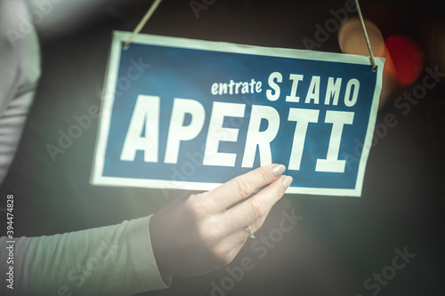 Close up of a females hand holding door sign ''come in, we are open'' in Italian