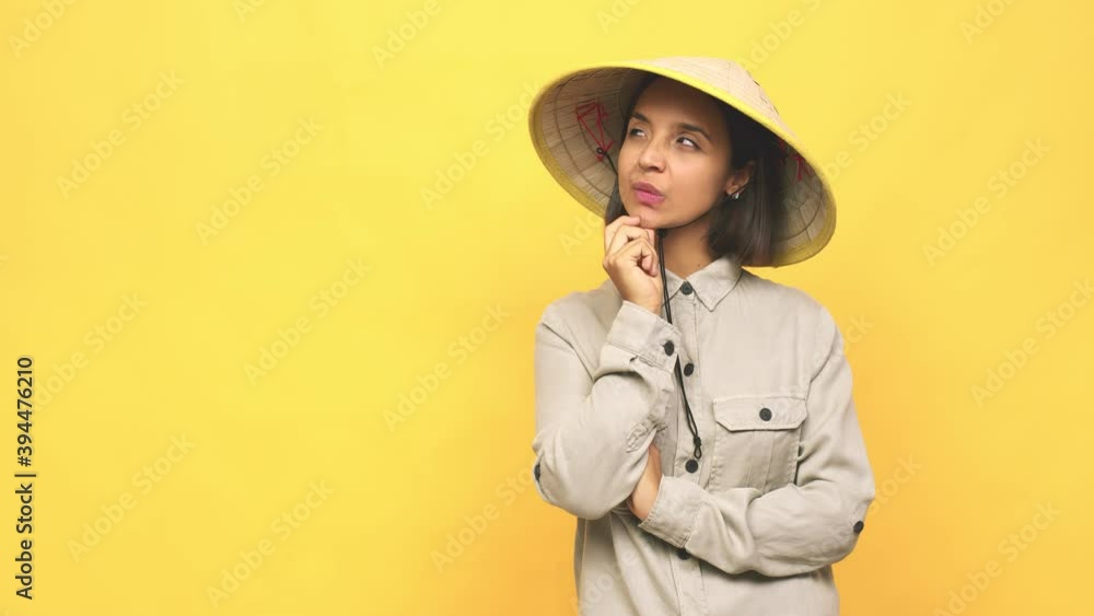 Young latin woman with vietnamite hat looking sideways with doubtful and skeptical expression Young latin woman with vietnamite hat looking sideways with doubtful and skeptical expression