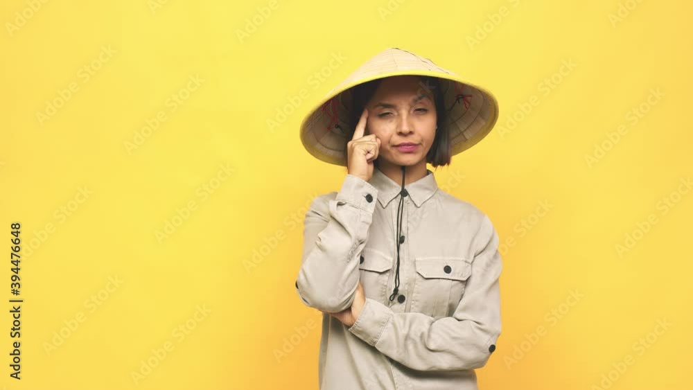 Young latin woman with vietnamite hat pointing temple with finger, thinking, focused on a task Young latin woman with vietnamite hat pointing temple with finger, thinking, focused on a task