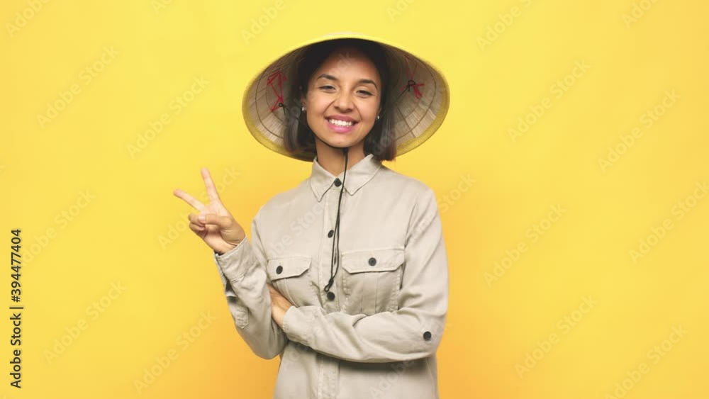 Young latin woman with vietnamite hat joyful and carefree showing a peace symbol with fingers Young latin woman with vietnamite hat joyful and carefree showing a peace symbol with fingers