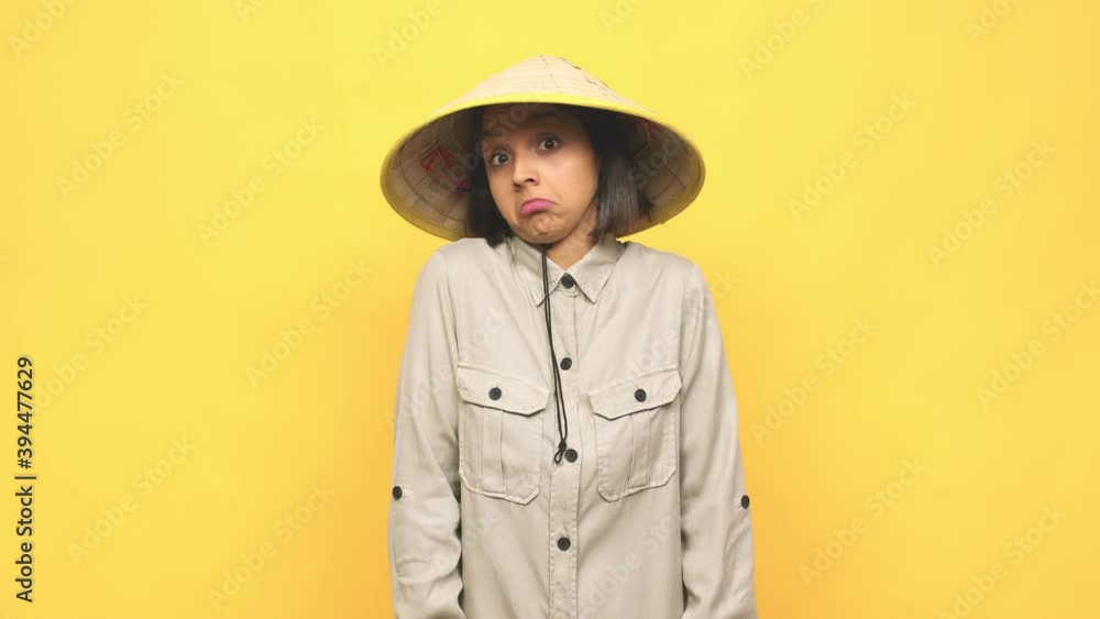 Young latin woman with vietnamite hat shrugs shoulders and open eyes confused Young latin woman with vietnamite hat shrugs shoulders and open eyes confused