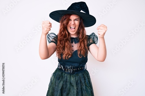 Young beautiful woman wearing witch halloween costume angry and mad raising fists frustrated and furious while shouting with anger. rage and aggressive concept. © Krakenimages.com