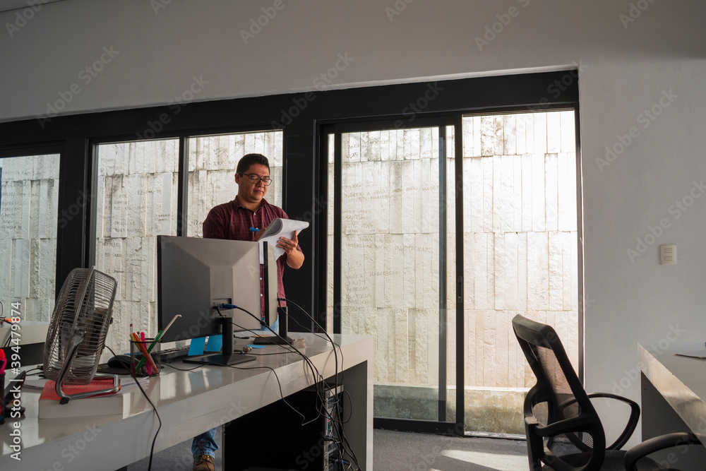A latin man with glasses, probably an architect or a entrepreneur writing in a notebook in a office, dressing informal clothes A latin man with glasses, probably an architect or a entrepreneur writing in a notebook in a office, dressing informal clothes
