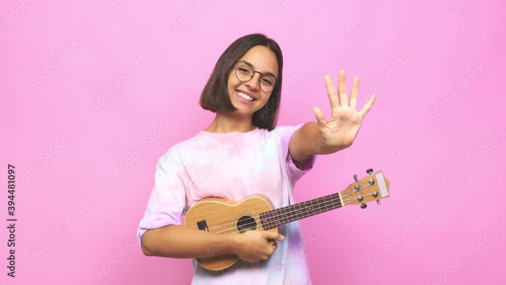 Young latin woman playing ukelele smiling cheerful showing number five with fingers Young latin woman playing ukelele smiling cheerful showing number five with fingers