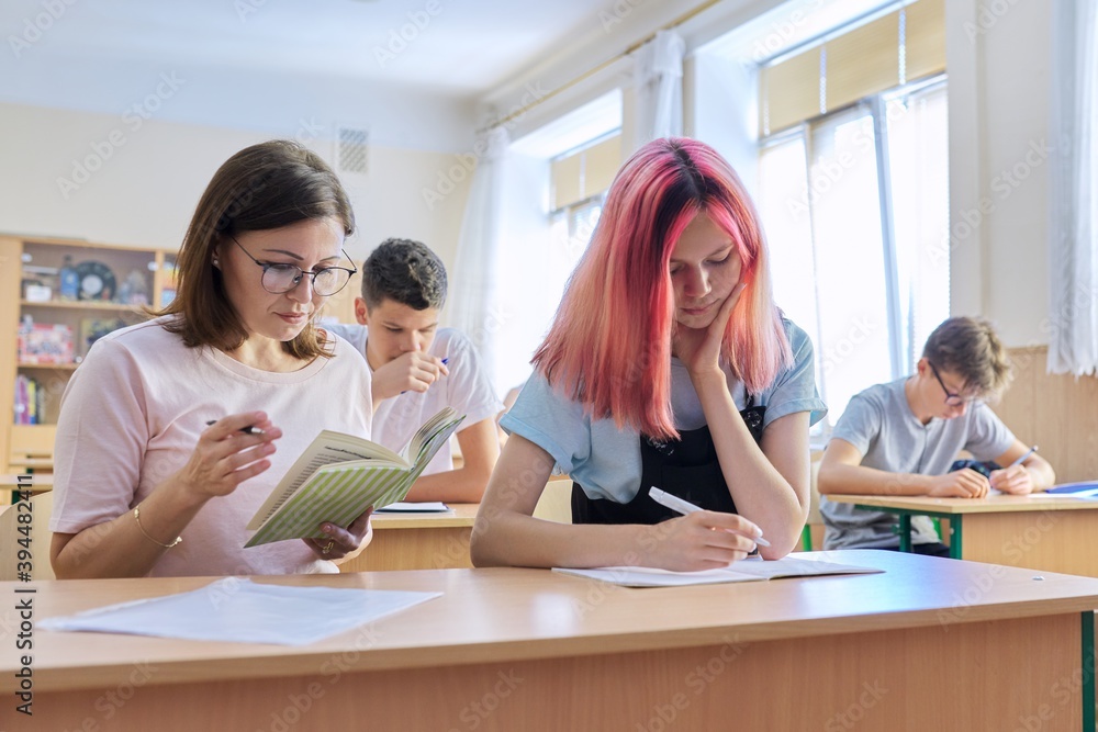 Middle-aged woman teacher sitting at desk with teenage student teaches Middle-aged woman teacher sitting at desk with teenage student teaches