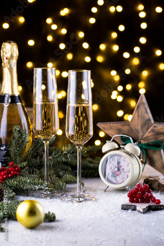 Two glasses of sparkling champagne at New year eve night with clock and bokeh background. Christmas decoration dinner table setting, copy space