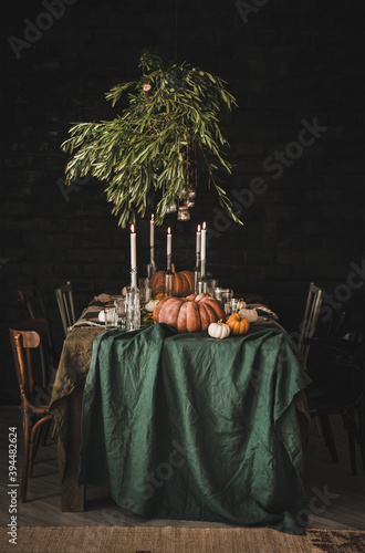 Stylish rustic Thanksgiving Day party table setting. Solid table with green linen tablecloth, dinnerware, glassware and cutlery decorated with pumpkins, glass candle holders and olive tree branches photo