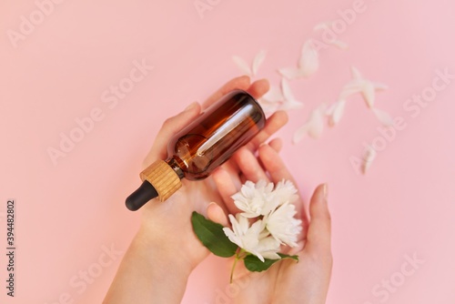 Woman s hands with flowers and cosmetic product in bottle  pink background