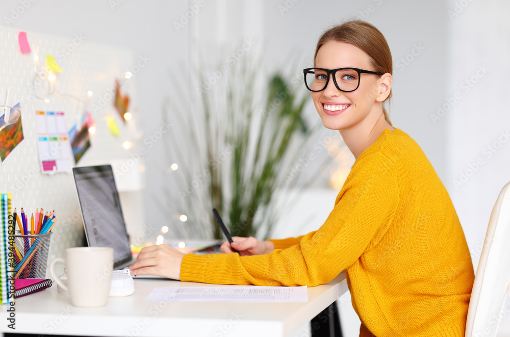 happy smiling freelancer woman in a yellow sweater works at computer at workplace with Christmas lights. happy smiling freelancer woman in a yellow sweater works at computer at workplace with Christmas lights.