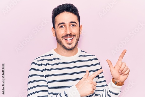 Young hispanic man wearing casual clothes smiling and looking at the camera pointing with two hands and fingers to the side.