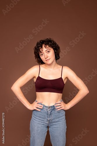 Young gorgeous brunette woman with short curly hair keeping her hands on waist