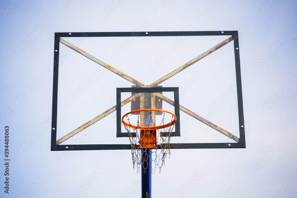 Basketball hoop with transparent board and chains instead of net against the light blue clear sky during the afternoon with a slight dark vignette on the side taken from a lower front angle Basketball hoop with transparent board and chains instead of net against the light blue clear sky during the afternoon with a slight dark vignette on the side taken from a lower front angle