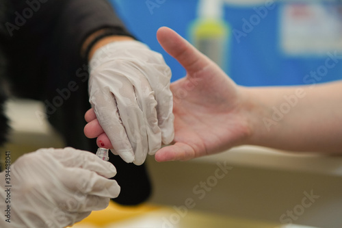 Close up of a medical nurse taking a blood sample from a finger of a patient into the vial while wearing a sterile gloves in the laboratory