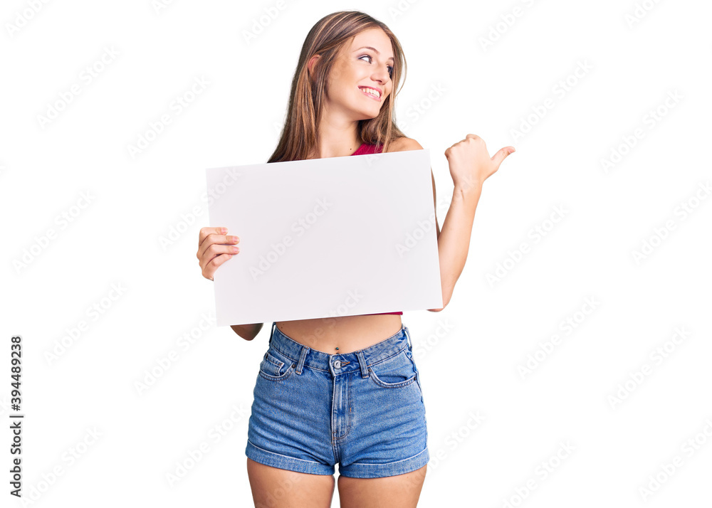Young beautiful blonde woman holding blank empty banner pointing thumb up to the side smiling happy with open mouth Young beautiful blonde woman holding blank empty banner pointing thumb up to the side smiling happy with open mouth