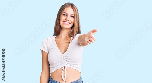 Young beautiful blonde woman wearing casual white tshirt smiling cheerful offering palm hand giving assistance and acceptance.