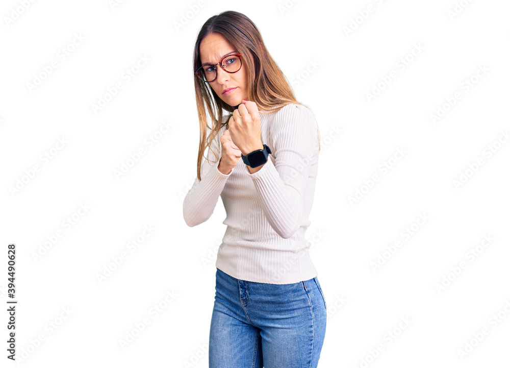 Beautiful brunette young woman wearing casual white sweater and glasses ready to fight with fist defense gesture, angry and upset face, afraid of problem Beautiful brunette young woman wearing casual white sweater and glasses ready to fight with fist defense gesture, angry and upset face, afraid of problem