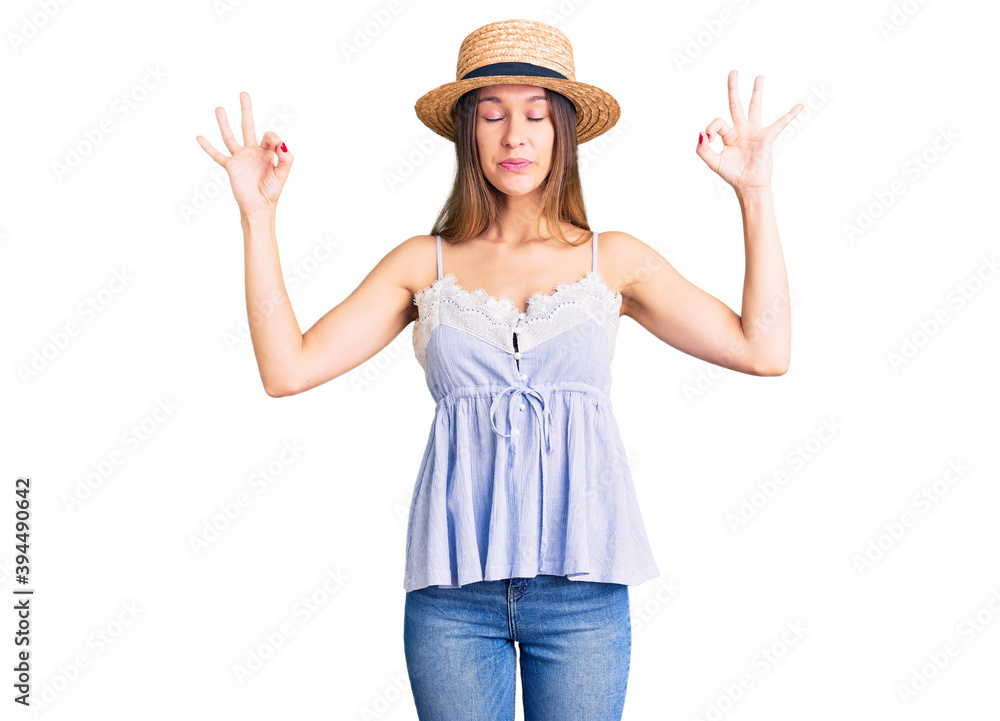 Beautiful brunette young woman wearing summer hat relax and smiling with eyes closed doing meditation gesture with fingers. yoga concept. Beautiful brunette young woman wearing summer hat relax and smiling with eyes closed doing meditation gesture with fingers. yoga concept.