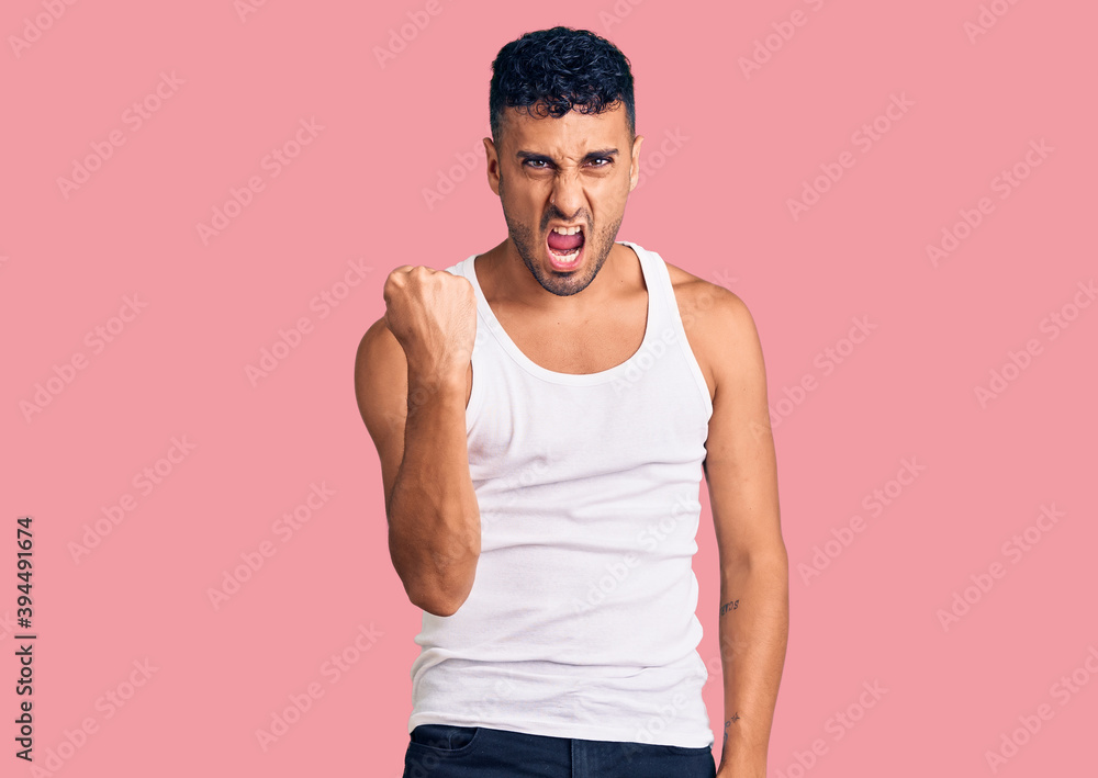 Young hispanic man wearing casual clothes angry and mad raising fist frustrated and furious while shouting with anger. rage and aggressive concept. Young hispanic man wearing casual clothes angry and mad raising fist frustrated and furious while shouting with anger. rage and aggressive concept.