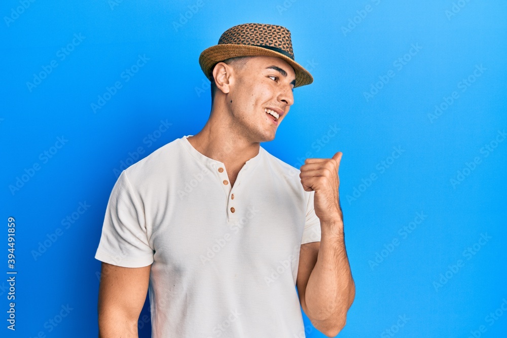 Handsome young man wearing summer hat smiling happy and positive, thumb up doing excellent and approval sign Handsome young man wearing summer hat smiling happy and positive, thumb up doing excellent and approval sign