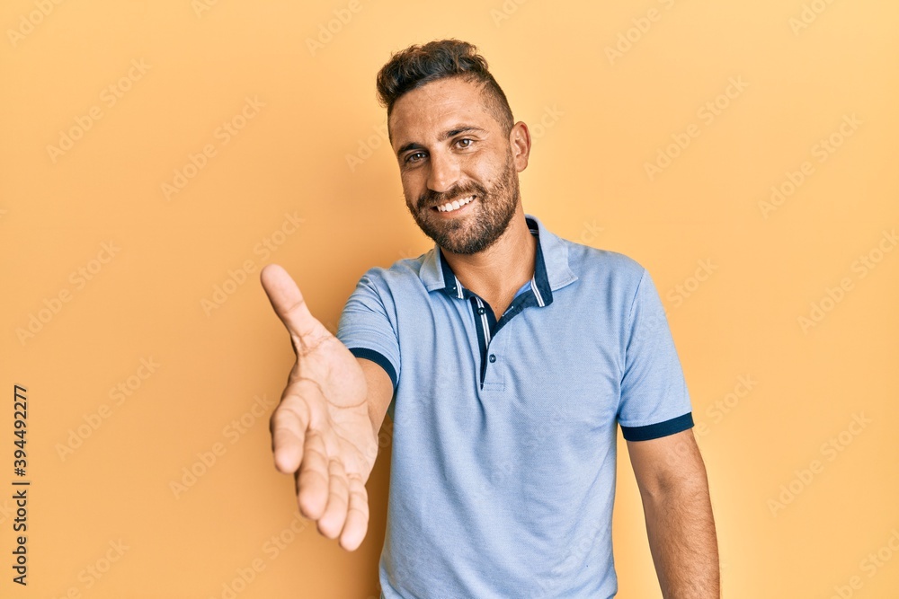 Handsome man with beard wearing casual clothes smiling friendly offering handshake as greeting and welcoming. successful business. Handsome man with beard wearing casual clothes smiling friendly offering handshake as greeting and welcoming. successful business.