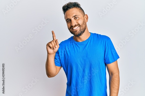 Handsome man with beard wearing casual clothes smiling with an idea or question pointing finger up with happy face  number one