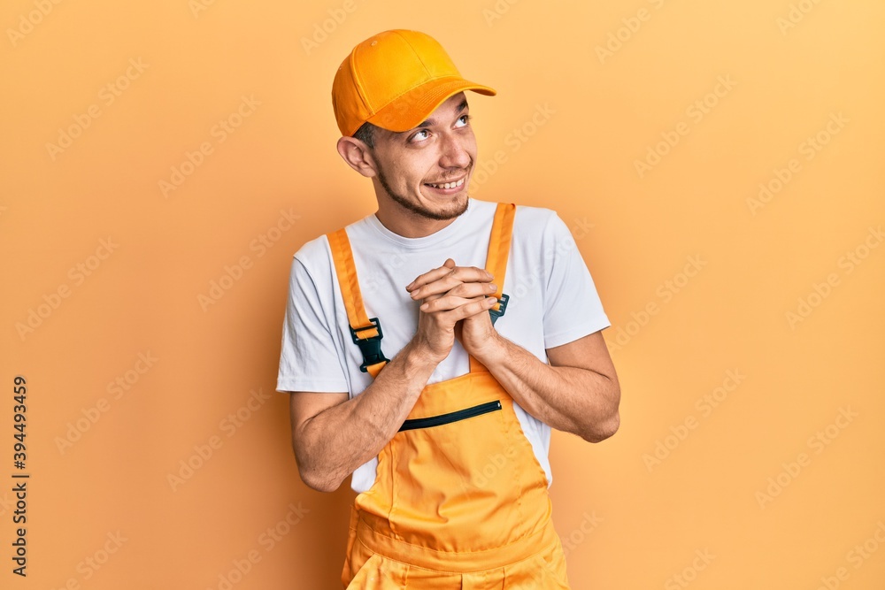 Young hispanic man wearing handyman uniform smiling pulling ears with fingers, funny gesture. audition problem Young hispanic man wearing handyman uniform smiling pulling ears with fingers, funny gesture. audition problem