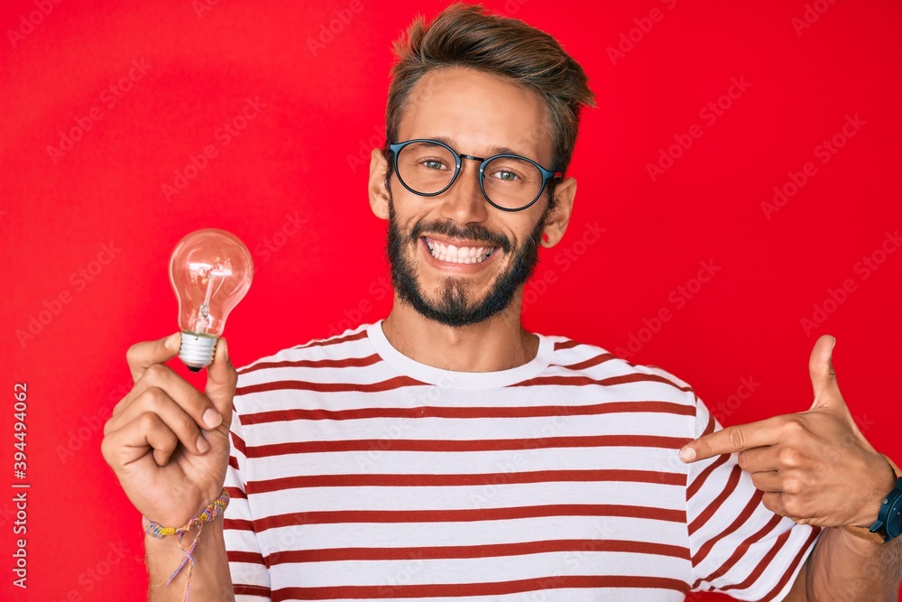 Handsome caucasian man with beard holding lightbulb for inspiration and idea pointing finger to one self smiling happy and proud Handsome caucasian man with beard holding lightbulb for inspiration and idea pointing finger to one self smiling happy and proud