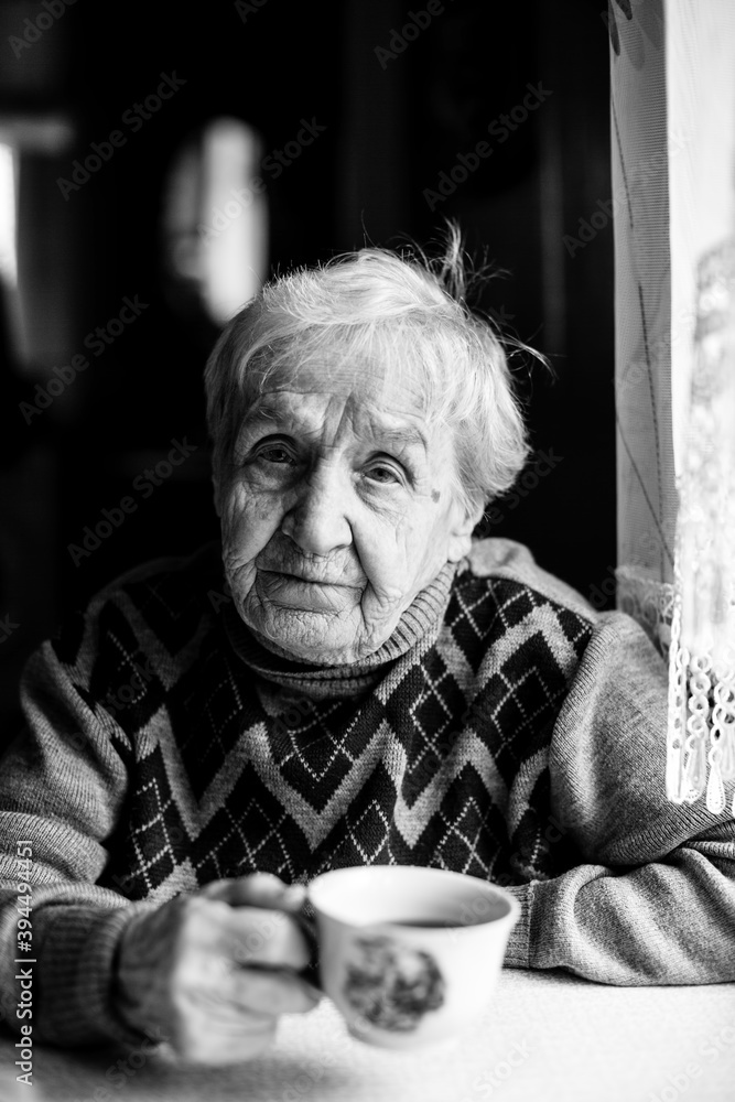 An old woman drinks coffee at home. Black and white photo. An old woman drinks coffee at home. Black and white photo.