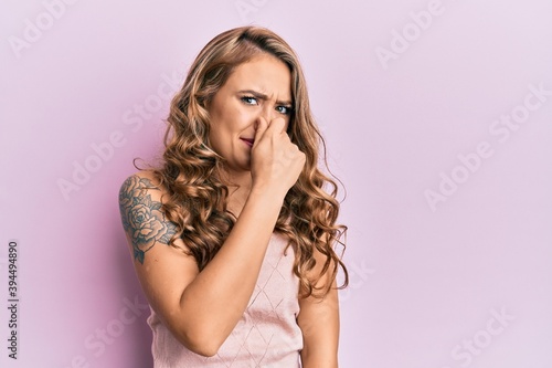 Young blonde girl wearing casual clothes smelling something stinky and disgusting, intolerable smell, holding breath with fingers on nose. bad smell