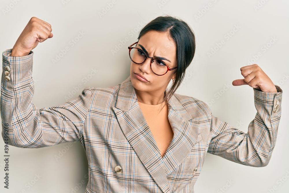 Young brunette woman wearing business jacket and glasses showing arms muscles smiling proud. fitness concept. Young brunette woman wearing business jacket and glasses showing arms muscles smiling proud. fitness concept.