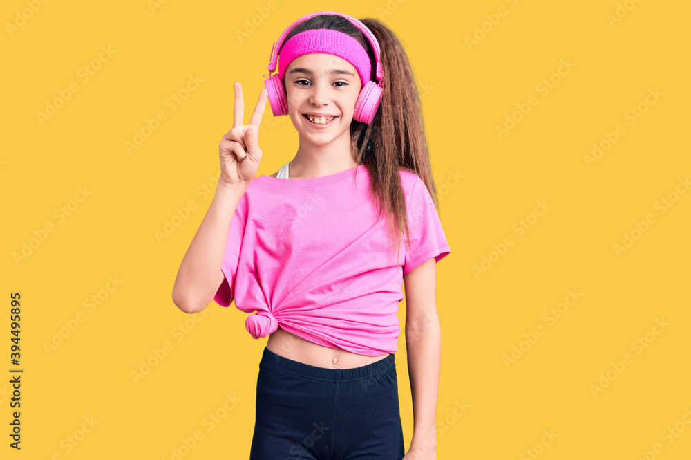 Cute hispanic child girl wearing gym clothes and using headphones showing and pointing up with fingers number two while smiling confident and happy. Cute hispanic child girl wearing gym clothes and using headphones showing and pointing up with fingers number two while smiling confident and happy.