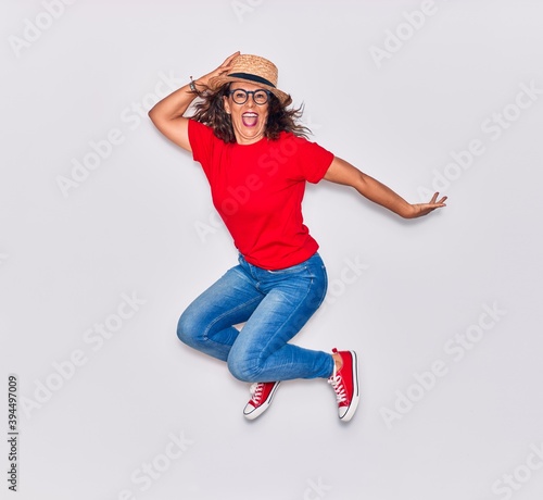 Middle age beautiful hispanic woman wearing casual clothes and hat smiling happy. Jumping with smile on face over white background