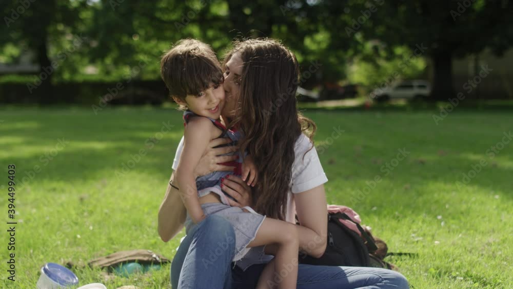 Portrait of a mother and son kissing each other on the cheek while sitting on the grass at a park Portrait of a mother and son kissing each other on the cheek while sitting on the grass at a park