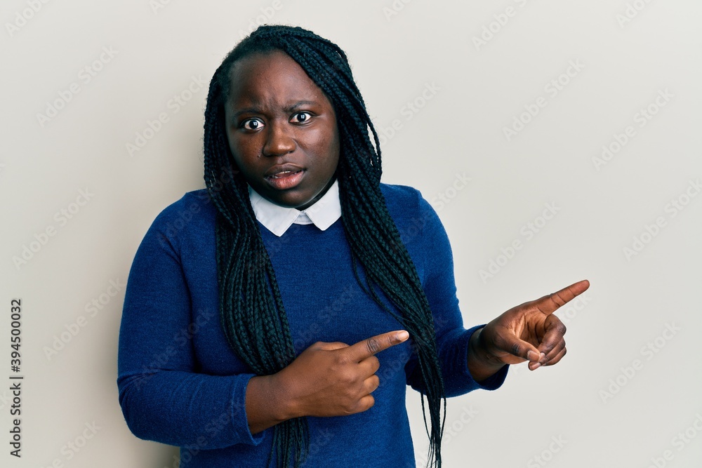 Young black woman with braids pointing up with fingers to the side in shock face, looking skeptical and sarcastic, surprised with open mouth Young black woman with braids pointing up with fingers to the side in shock face, looking skeptical and sarcastic, surprised with open mouth