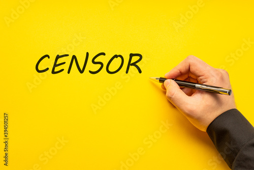 Male hand writes in black pen the word censor on a yellow background with copy space. Business concept photo photo