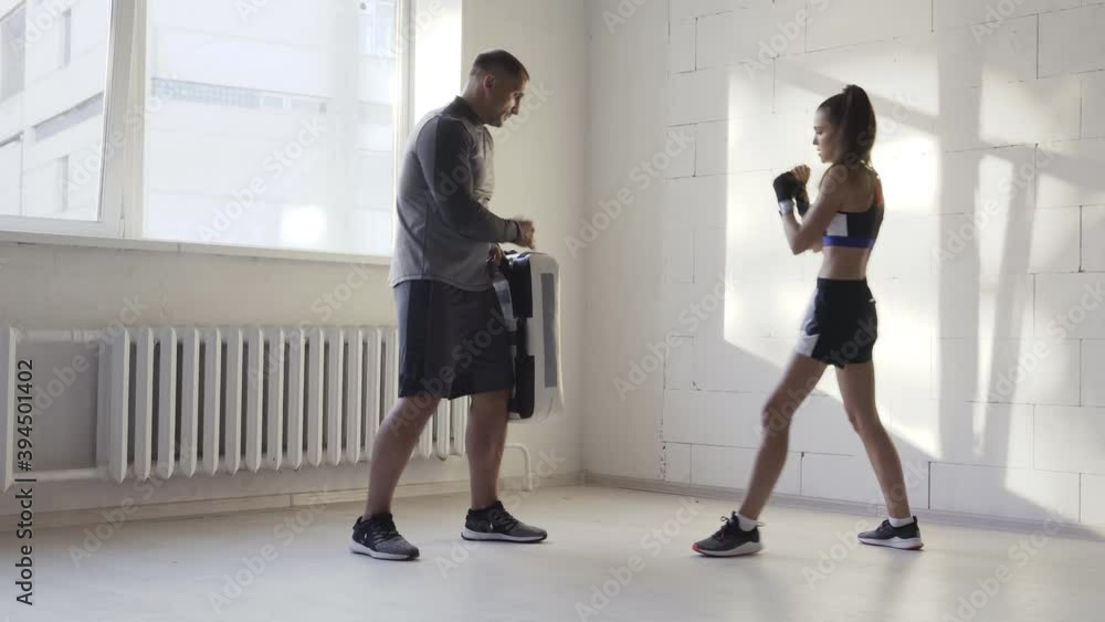 Female martial arts fighter practicing leg kick or low kick with her trainer in a boxing studio at sunny day. Female martial arts fighter practicing leg kick or low kick with her trainer in a boxing studio at sunny day.
