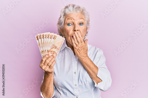 Photography Senior grey-haired woman holding 50 turkish lira banknotes covering mouth with hand, shocked and afraid for mistake
