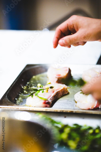 Professional cook puts salt and green ingredients in fish dish