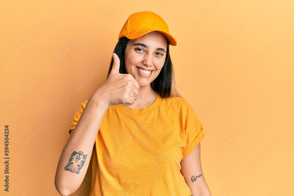Young hispanic woman wearing delivery uniform and cap amazed and smiling to the camera while presenting with hand and pointing with finger. Young hispanic woman wearing delivery uniform and cap amazed and smiling to the camera while presenting with hand and pointing with finger.